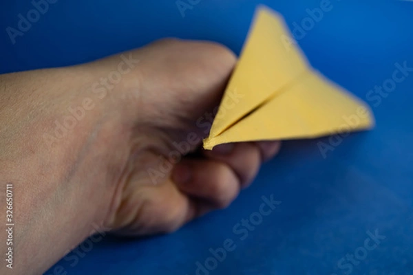 Fototapeta Hand holds paper yellow airplane. Blurred background