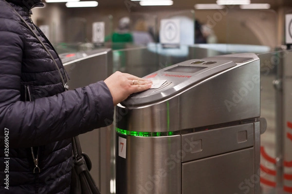 Fototapeta A woman in a jacket with a bag over her shoulder and a wedding ring on her finger applies a ticket to a sensor of an automatic subway system in Moscow. Translation: pass.