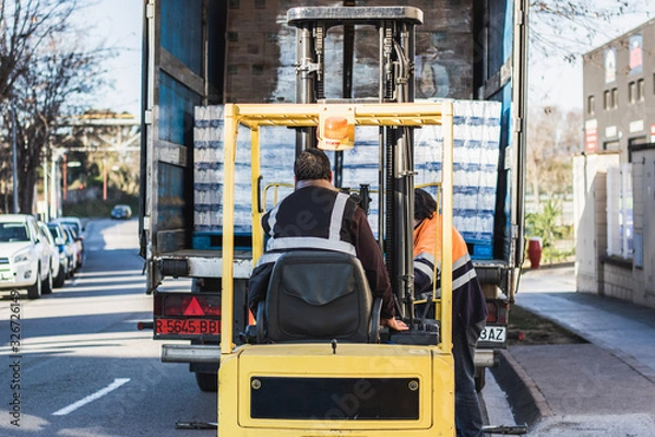 Fototapeta Man with forklift loading boxes and riding them in a truck