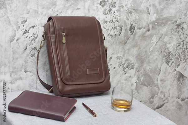 Fototapeta Leather business bag and accessories in the work room with gray concrete wall, wood table and leather chair.