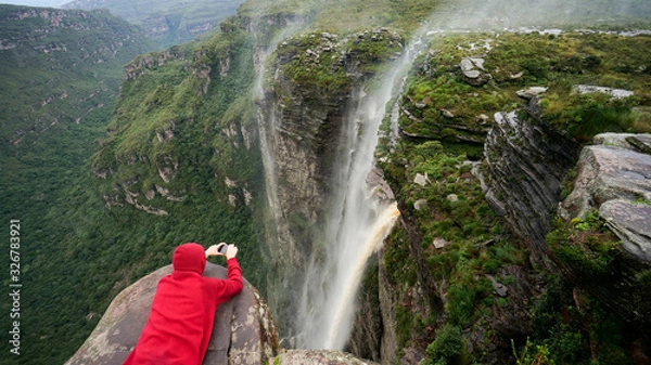 Obraz Traveler lies on the edge of the cliff and taking a picture of the waterfall in Chapada Diamantina national park, State of Bahia, Brazil.