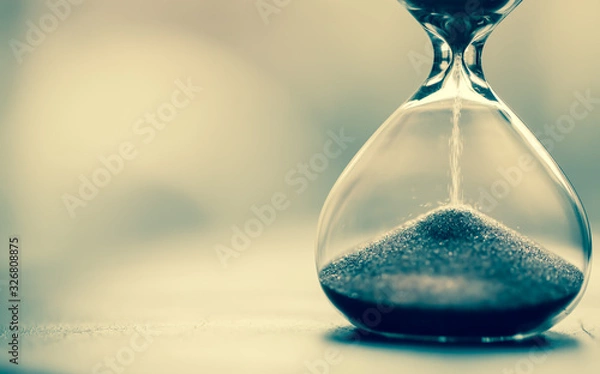 Fototapeta Sand running through the bulbs of an hourglass measuring the passing time in a countdown to a deadline, on a bright background with copy space.