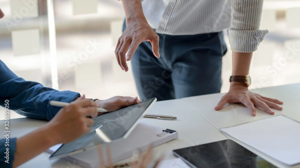 Fototapeta Cropped shot of businesspeople consulting on their project with digital tablet and document file