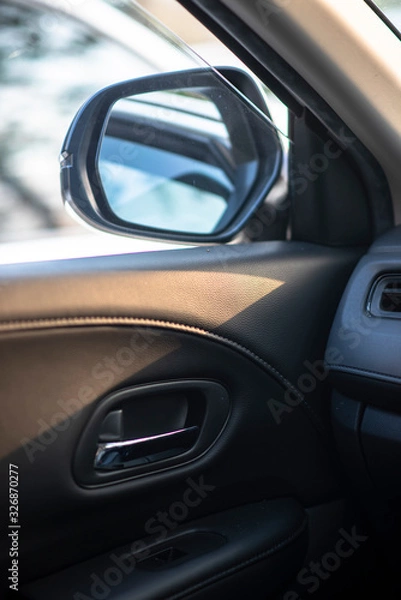 Fototapeta Folded wing mirror of a compact modern car, with a side window glass drop down for ventilation, seeing an inner car door handle. Car parked in a parking lot during the morning time with sun rise.
