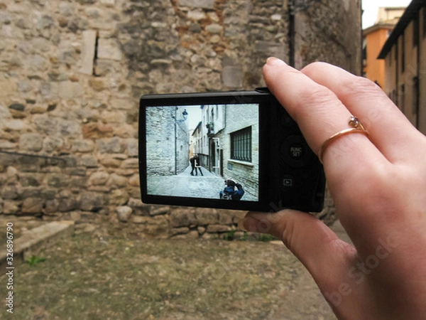 Obraz A hand holding a camera with a picture on the screen: an outdoor photographer taking a picture of a young couple standing in the ancient street