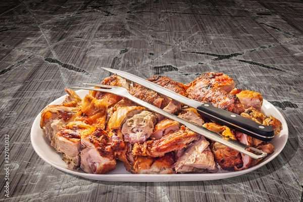 Fototapeta Freshly Spit Roasted Pork Meat Slices Offered on Oblong Porcelain Tray with Carving Knife and Serving Fork Set on Old Weathered Rustic Picnic Table Vignette Backdrop