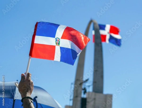 Fototapeta A hand holding the Dominican flag with the monument in the background
