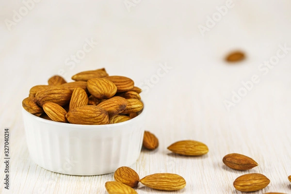 Obraz Almonds in a white bowl and on a white wooden surface