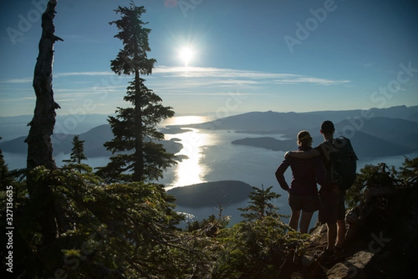Obraz COUPLE STANDING on the top of mountain overlooking islands during sunset in beautiful British Columbia Vancouver Canada after hike in forest