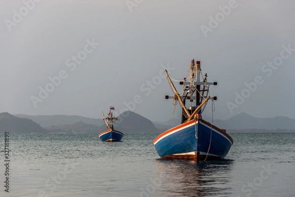 Fototapeta two small Thai fisherman boats in the Thai national colours red, white and blue anchoring in the sea with some mountains in the distant background