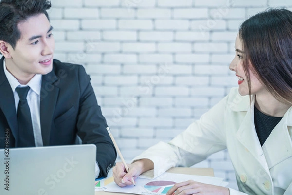 Fototapeta Smiling Asian business woman hold pecil, take note while listening to suggestions from manager. Smart coworkers discuss, brainstorm for operating performance report. Communication and business concept