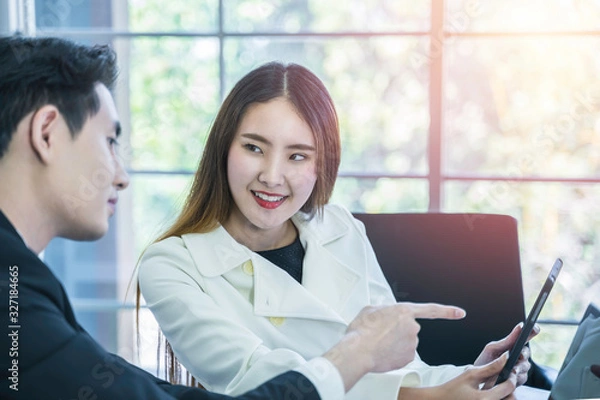 Fototapeta Smiling Asian business woman listening colleague comment and pointing at tablet in meeting. Smart coworkers discuss, brainstorm for new project planning. Communication and business concept, Daylight