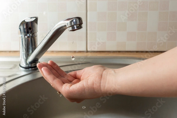 Obraz A drop of water drips from faucet in human palm above round metal kitchen sink