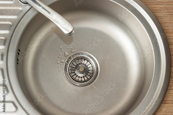 Fototapeta Drops on the bottom of clean round metal kitchen sink with a leaking tap