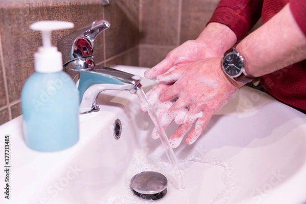 Fototapeta Man is washing his hands with a soap in a bathroom. Washing hands with soap under the faucet with water.