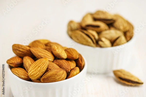 Obraz Two white bowls with peeled and unpeeled almonds on a white surface