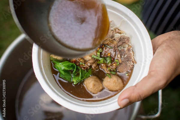 Fototapeta pouring soup with a ladle in a bowl with Thai beef noodle soup (ก๋วยเตี๋ยวเนื้อน้ําใส)