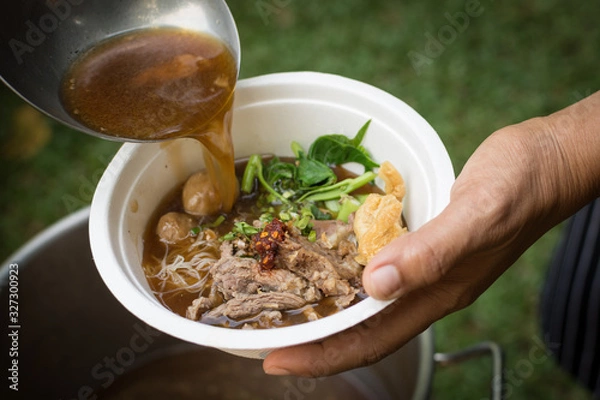 Obraz pouring soup with a ladle in a bowl with Thai beef noodle soup (ก๋วยเตี๋ยวเนื้อน้ําใส)