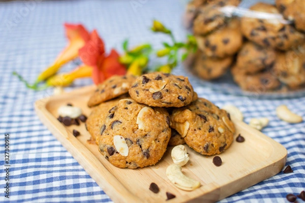 Fototapeta closeup of chocolate chip and nuts cookies decorated on a wooden plate with a cookie jar and flowers on a blue and white checked table cloth