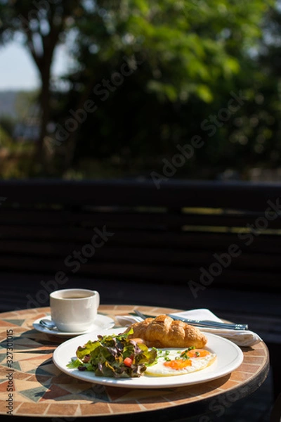 Obraz breakfast with croissant, sunny side up eggs, salad and coffee served on a round table in the garden