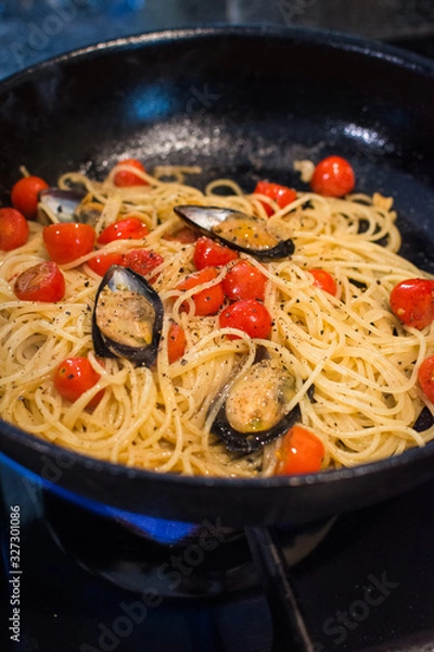 Obraz closeup of spaghetti Vongole with roma tomatoes and mussels beeing heated in a pan on a gas stove