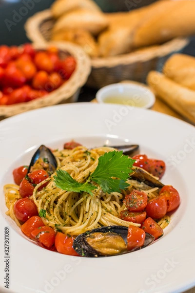 Fototapeta closeup of spaghetti Vongole with roma tomatoes and mussels served and decorated on a plate with tomatoes, bread and olive oil in the background