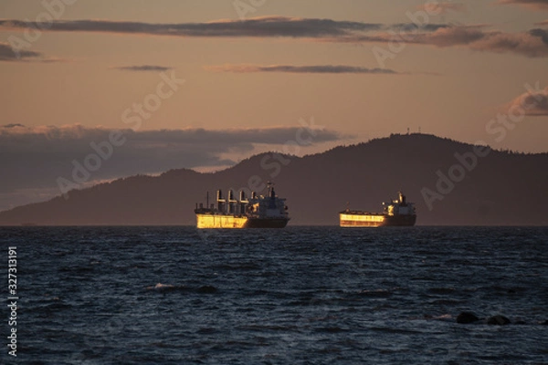 Obraz LARGE CARGO SHIPS AWAITING WAITING to get loaded on a coast during sunset golden hour in between mountains with scenic view at pacific ocean Pacific north west Vancouver Canada British Columbia 