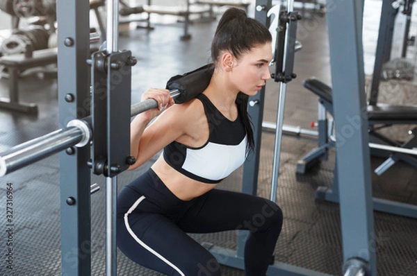 Fototapeta Young woman doing exercises with barbell in gym