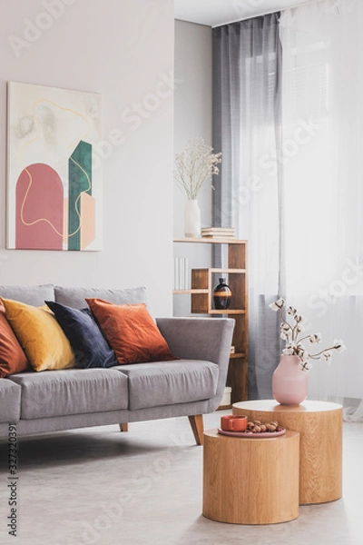 Fototapeta Flowers in pastel pink vase on wooden coffee table in front of grey scandinavian couch with colorful pillows