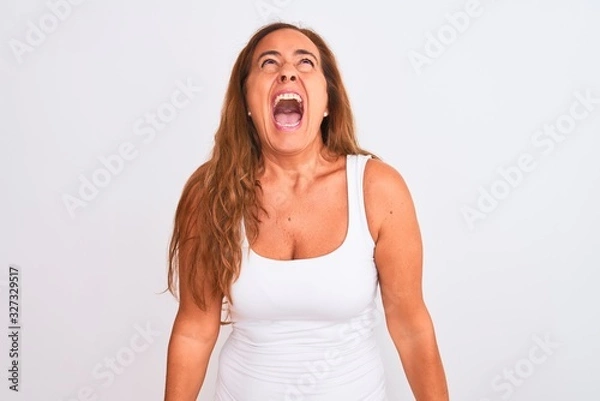 Fototapeta Middle age mature woman standing over white isolated background angry and mad screaming frustrated and furious, shouting with anger. Rage and aggressive concept.