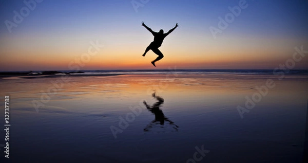 Fototapeta Silhouette of a jumping man on the beach by the ocean