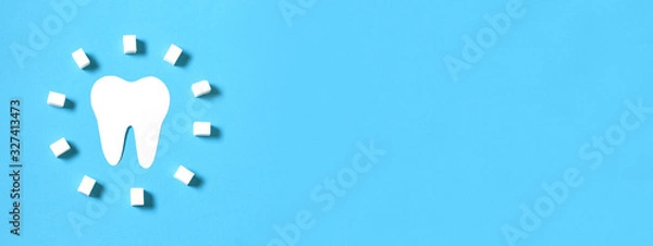 Fototapeta Paper tooth figurine and circle sugar cubes on a blue background. Caries tooth problems