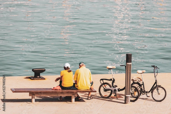 Fototapeta Older couple sitting in the harbor next to their bikes
