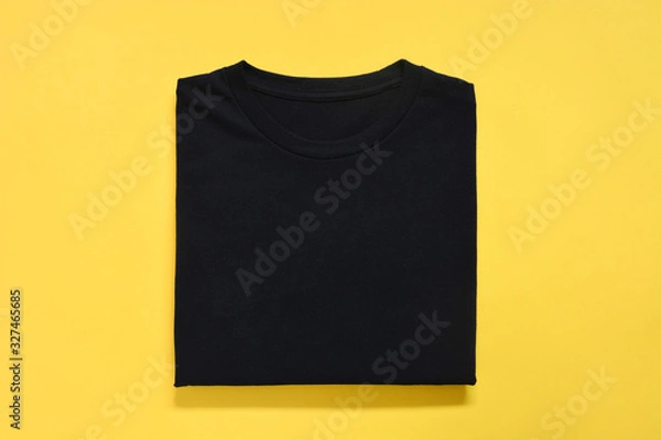 Fototapeta top view of folded black color t-shirt on yellow background, copy space, flat lay