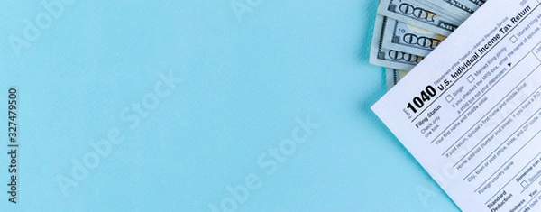 Fototapeta Tax time concept. Still life of US individual Income Tax Form 1040 with several 100 dollar banknotes on a wide blue pastel background with copy space.