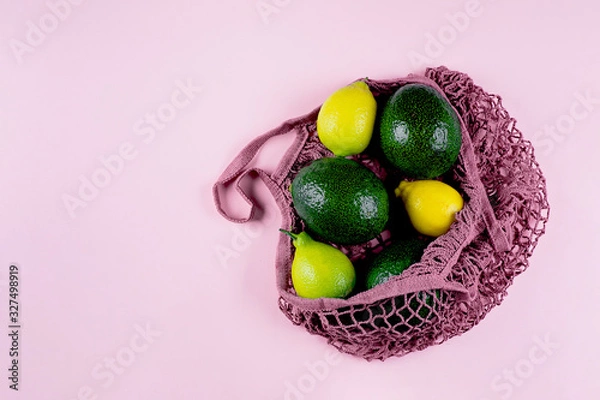 Fototapeta Mesh shopping bag with lemons and avocado on pink background. Top view, flat lay, copy space. Zero waste, eco friendly concept.