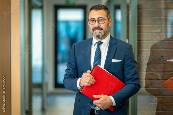 Obraz A charismatic, bespectacled bank employee takes notes on his red file