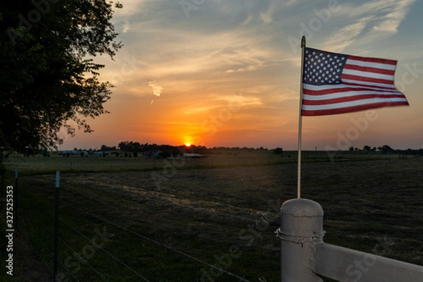 Fototapeta An american flag on the fence of a farm near the city of Commerce in the State of Oklahoma, at sunset, USA.
