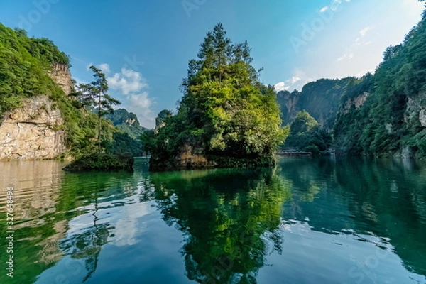 Obraz Small island covered with vegetation in the center of a lake with green waters and rugged mountains in the background. Baofeng Lake (Bao Feng Hu) in Suoxi Valley, Wulingyuan, China