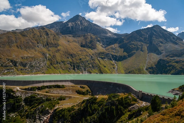 Obraz A view of the Alpine dam at the foot of the rocky peaks under the blue sky with nice clouds