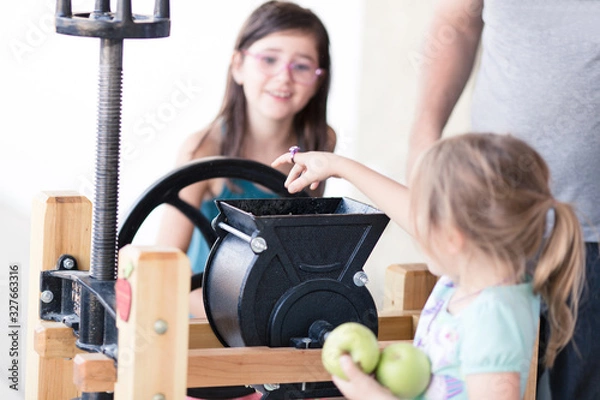 Obraz Kids are helping make fresh apple cider with an apple cider press.