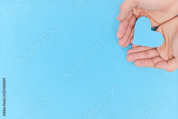 Fototapeta Hands holding a blue heart in blue background. Top view with copy space.