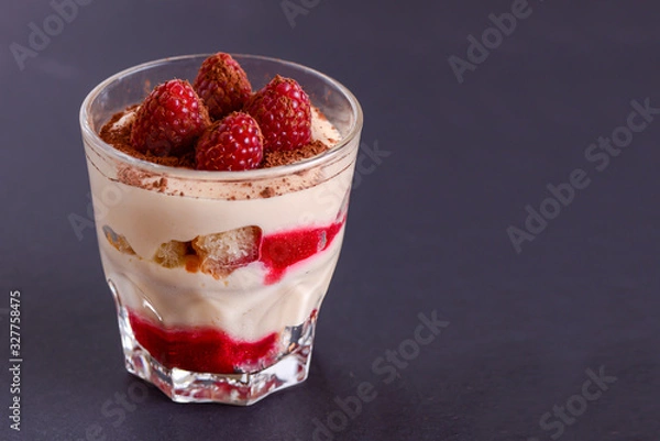 Fototapeta Italian dessert panna cotta with raspberries and cocoa powder served in small glass over black background.