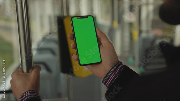 Obraz NEW YORK - May 19, 2019: Slow motion man young hand uses holding a mobile telephone with a vertical green screen background tram inside window key smartphone technology touch message display close up