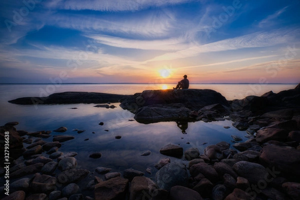 Obraz Man sitting on a cliff by a lake during sunset