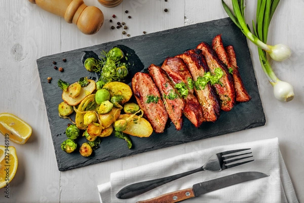 Obraz Medium rare meat hanger steak with brussels sprouts, potatoes and onion with herb sauce on a white wooden table. Delicious healthy food. Top view above.