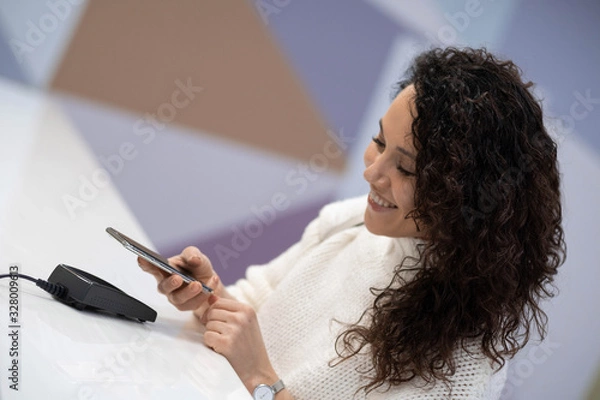 Obraz A cheerful beautiful woman pays for a service in a medical clinic using her phone