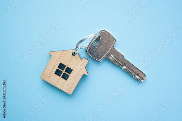 Fototapeta Key and house shaped keychain arrangement on blue background. Top view, flat lay. Real estate, insurance concept, mortgage, buy sell house, realtor concept.