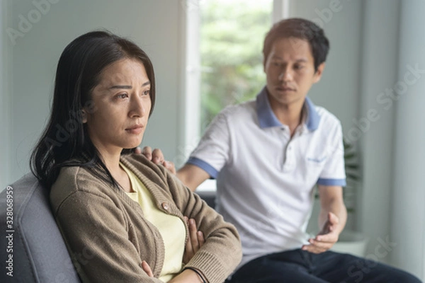 Fototapeta Asian couple having relation problem. Wife crying and sitting separate with her husband at home after quarrel.