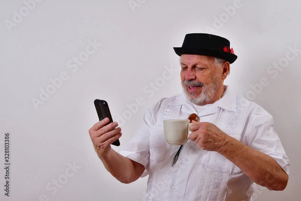Fototapeta Smiling old man talking on the phone and having a cup of coffee..Elderly gentleman taking a coffee break and talking on his cellphone.Senior man enjoying a hot cup of coffee and talking on the phone..